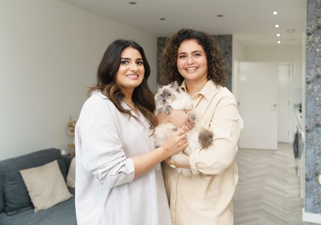Two women standing in their living-room holding their cat