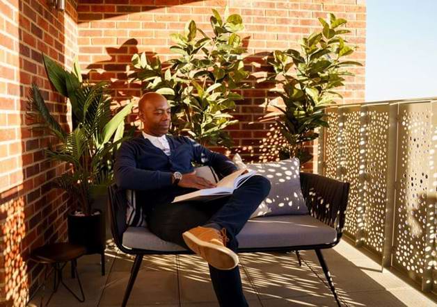 man reading a book while sat on his balcony