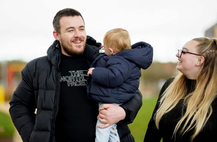 man standing outside holding his child next to the mom